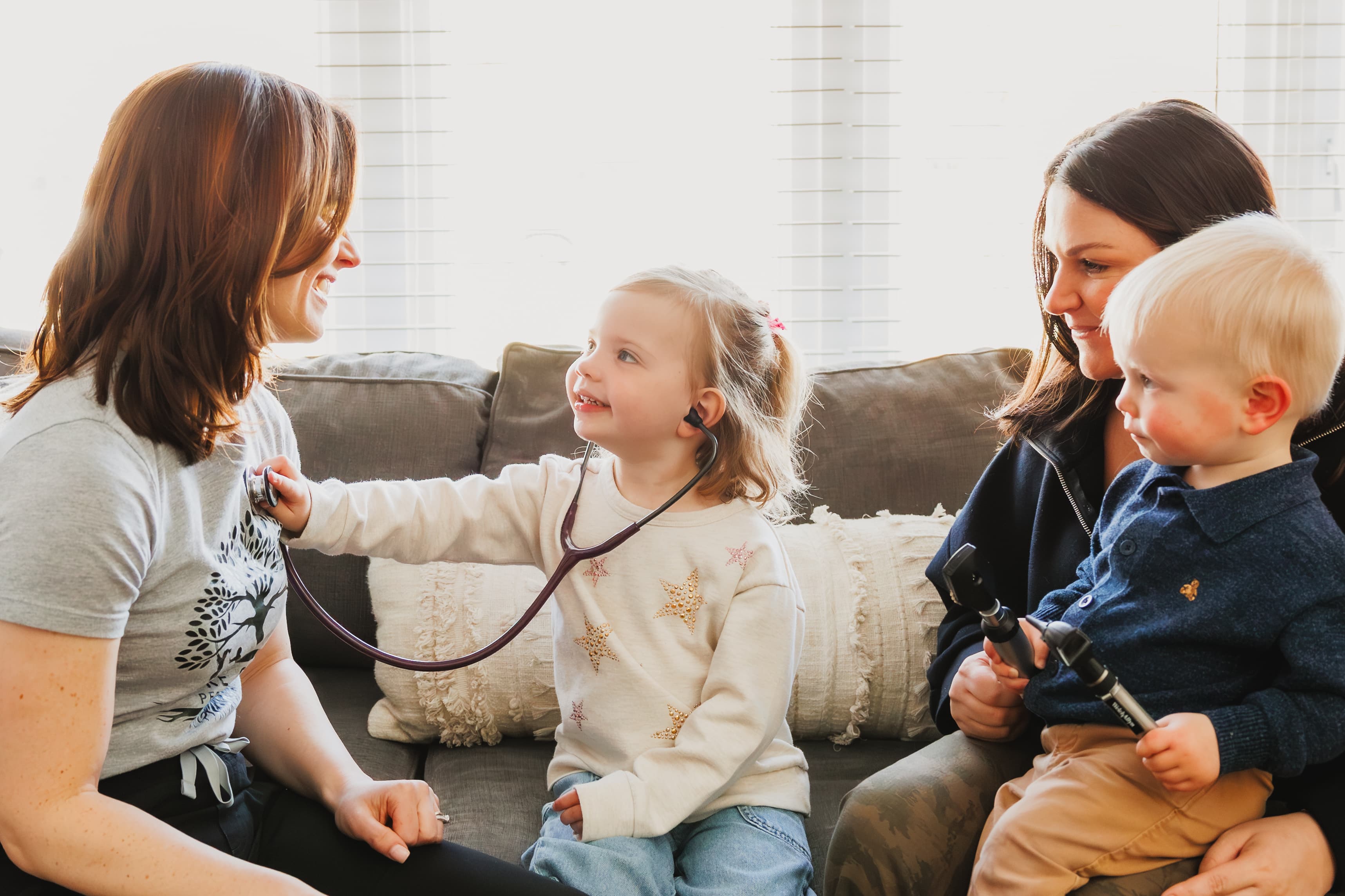 Pediatrician using a stethoscope with a smiling young girl during a relaxed home visit on Long Island